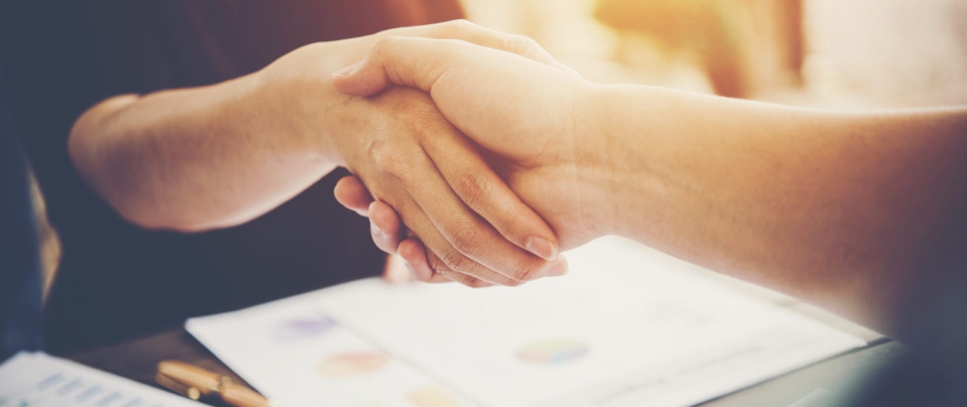 Close-up of two business people shaking hands while sitting at the working place.